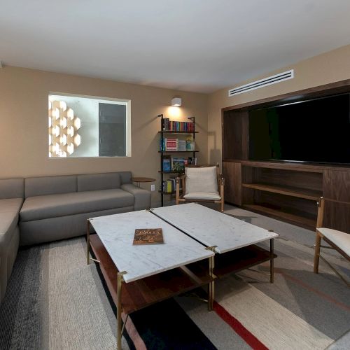 A modern living room with a sectional sofa, coffee table, wall art, and a sleek kitchen area in the background, all in a neutral color palette.