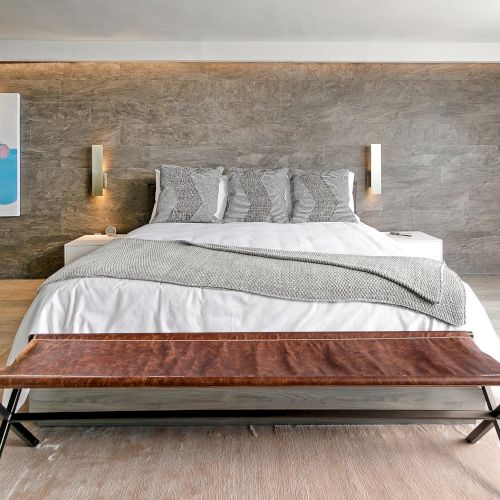 A neatly made bed with white and rust-colored bedding, a wooden floor, and simple wall decor.