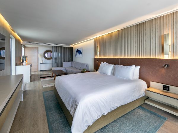 A modern hotel room with a large bed, soft lighting, wood-accent wall, seating area, and a desk; clean, airy, and stylish.