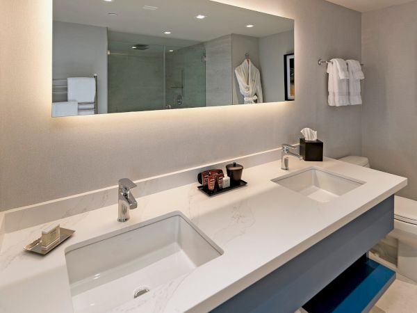 A modern bathroom vanity with a large mirror, double sinks, and a backlit edge; items like soap, towels, and storage baskets on and beneath the counter.