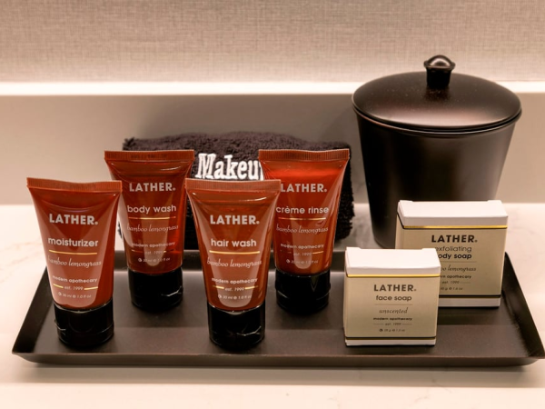 A tray with Lather toiletries&mdash;body wash, hair wash, moisturizer, and cream rinse&mdash;plus small soaps and a black pot in the background.