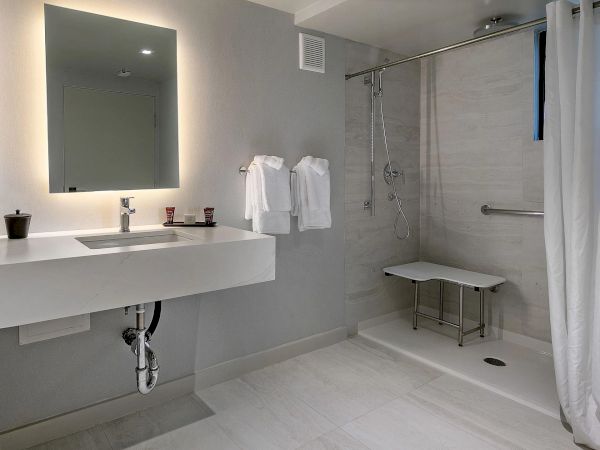 Modern bathroom with a floating sink, large mirror, towel rack, and a spacious walk-in shower with a bench and curtain.