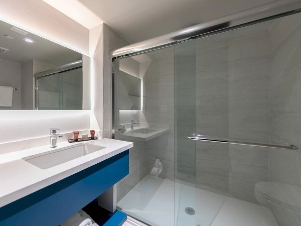 A modern bathroom with a white sink, blue vanity, large mirror, and a glass shower enclosure with a sliding door.