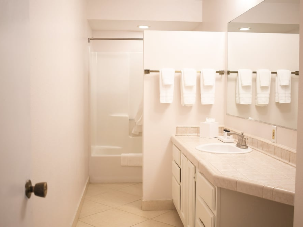 A clean bathroom with a long marble countertop, sink, mirror, and towels neatly arranged on a rack above the vanity in a bright, airy space.