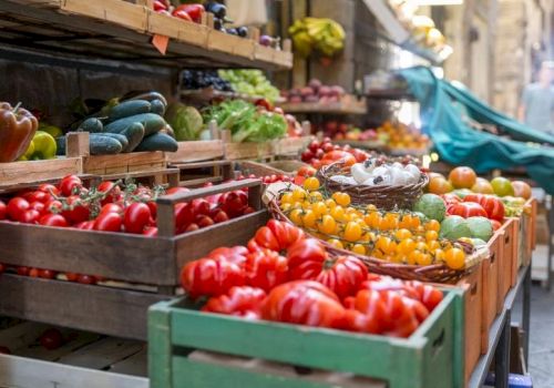 A colorful outdoor market stall filled with vibrant tomatoes, peppers, and peppers in wooden crates, with fresh produce and a bustling vibe.