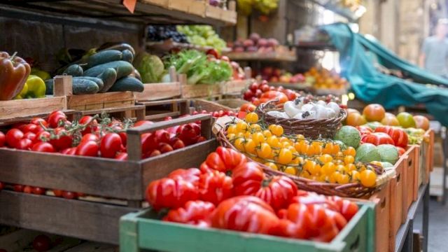 A colorful outdoor market stall filled with vibrant tomatoes, peppers, and peppers in wooden crates, with fresh produce and a bustling vibe.