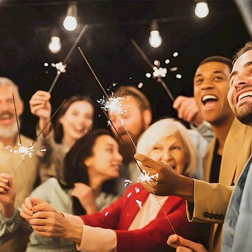 A diverse group of friends celebrating with sparklers at a night party, smiling and cheering as they shine festive lights together.