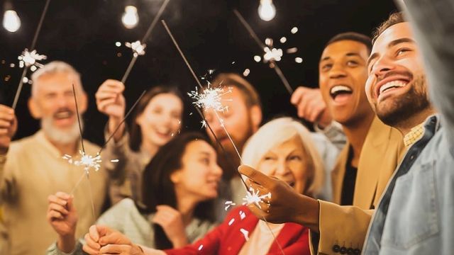 A diverse group of friends celebrating with sparklers at a night party, smiling and cheering as they shine festive lights together.