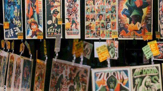 A display of vintage comic book covers and pages hanging for sale, colorful artwork with superhero and character panels, tags attached.