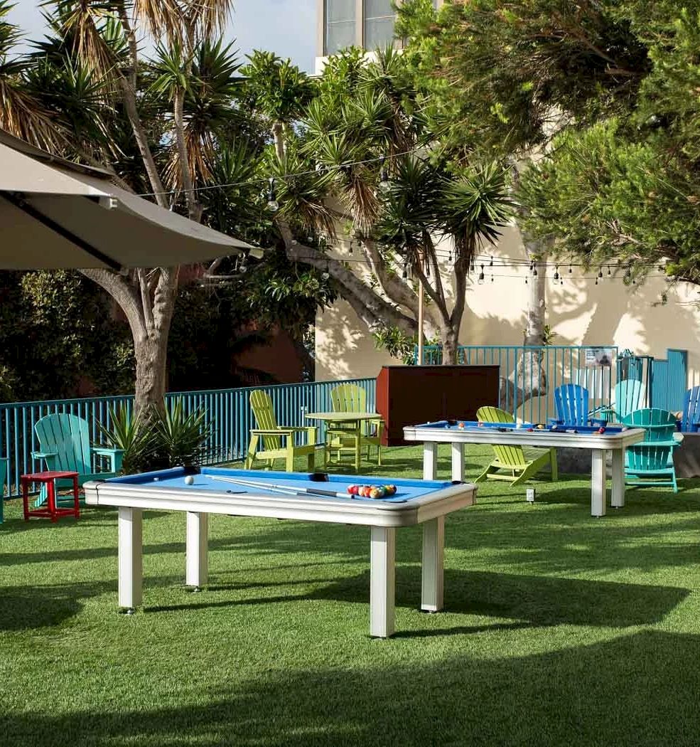 A sunny outdoor setup with colorful plastic chairs around a white table, a shaded area, trees, and a well-kept lawn, perfect for a casual gathering.