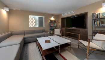A modern living room with a gray L-shaped sofa, white coffee table, a large wall-mounted TV, mid-century chairs, and bookshelves.