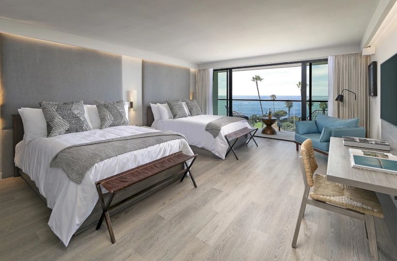 A bright hotel room with two queen beds, a desk, and a balcony with ocean view. Ends with a period.