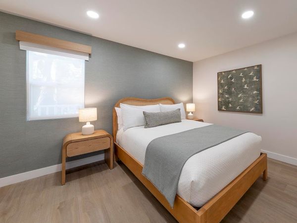 A clean, modern bedroom with a wooden bed, two nightstands, soft lighting, and a calming gray-blue accent wall.