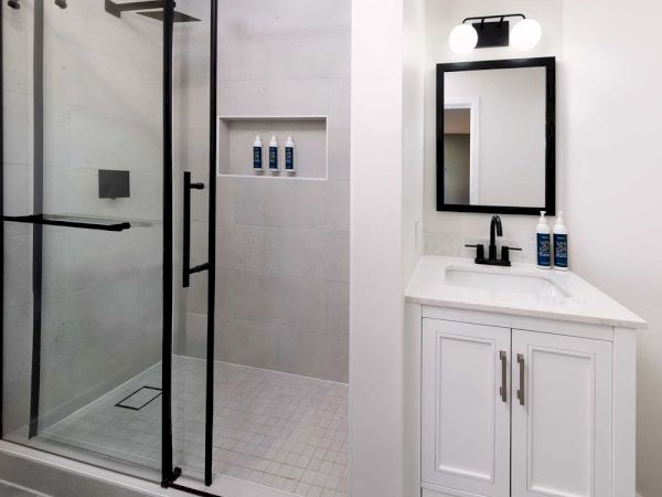A modern bathroom with a glass-enclosed shower, white vanity with a black faucet, and a framed mirror; minimalist, monochrome, clean lines.
